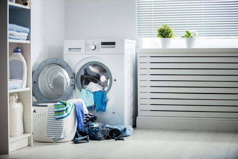 A laundry room with washer, dryer, clothes, towels, and a potted plant.