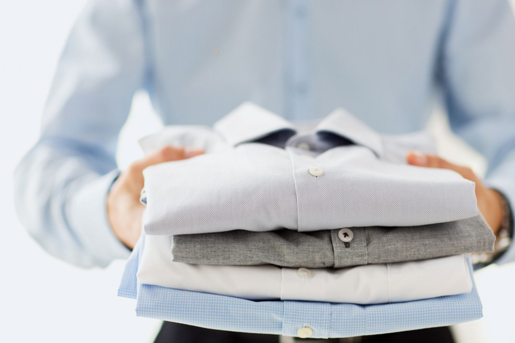 A person holding a stack of neatly folded white shirts in their hands, preparing to put on a shirt or organize their wardrobe.