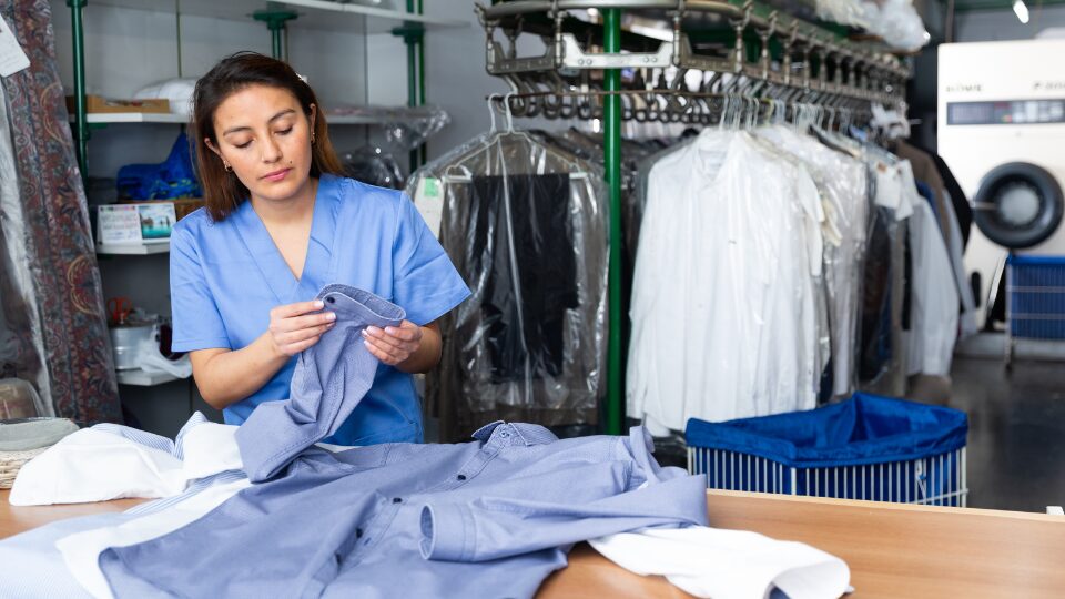 Focused woman dry-cleaning worker checking clean clothes
