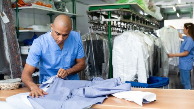 Confident man dry-cleaning worker checking clean clothes