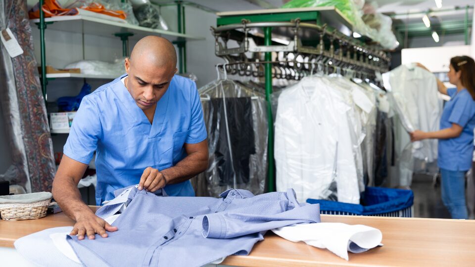Confident man dry-cleaning worker checking clean clothes